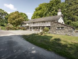 A stone and white two-story house with wooden balcony surrounded by trees and grass at High Lindeth in Bowness
