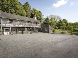 A stone and white two-story house with a balcony and gravel driveway surrounded by trees at High Lindeth in Bowness