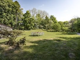 An outdoor grassy area with a table and chairs surrounded by trees at High Lindeth in Bowness