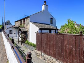 A stone and white plaster cottage with a wooden fence and a stone pathway at The Cottage in Keswick