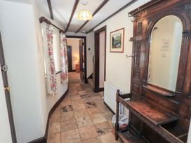 A hallway with tiled floor floral curtains on windows a wooden coat rack with a mirror and an open door leading to another room at The Cottage in Keswick