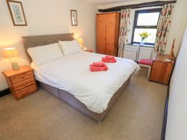 A bedroom with a double bed, two bedside tables with lamps, a wooden wardrobe, a desk with a red chair, and a window with floral curtains at The Cottage in Keswick