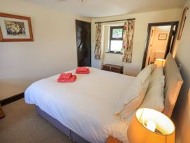 A bedroom with a double bed with white bedding and two red towels on it a wooden chest under a window with floral curtains and a lamp on a bedside table at The Cottage in Keswick