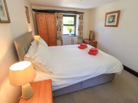 A bedroom with a bed with white linens and red towels a wooden wardrobe a dresser with a mirror and a lamp on a bedside table at The Cottage in Keswick