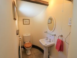 A small bathroom with a toilet and sink a round mirror and a pink towel at The Cottage in Keswick