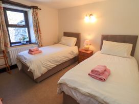 A bedroom with two single beds a nightstand with a lamp and a window with floral curtains at The Cottage in Keswick