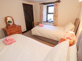 A bedroom with two single beds, a wooden dresser with mirror, a window with floral curtains, a lamp, and pink towels on beds at The Cottage in Keswick