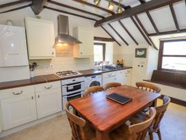 A kitchen with wooden table and chairs next to white cabinets under a ceiling with exposed beams at The Cottage in Keswick