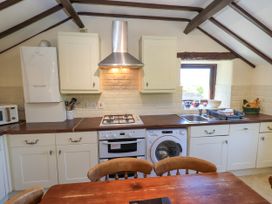 A kitchen with white cabinets a gas stove oven washing machine microwave and wooden dining table at The Cottage in Keswick