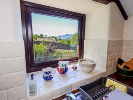 A kitchen window with ceramic pitchers and a bowl on the sill and a dish rack by the sink at The Cottage in Keswick