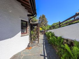A stone pathway next to a white house wall with a wooden gate and green plants at The Cottage in Keswick