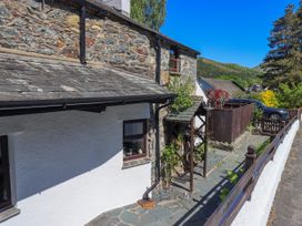 A stone and white plaster house with a slate roof a wooden trellis with climbing plants a paved walkway and a parked car behind a wooden fence at The Cottage in Keswick