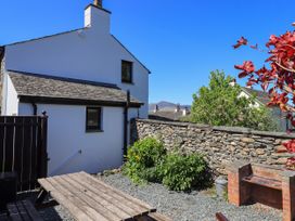 A backyard with a wooden picnic table a brick barbecue stone wall and a white house at The Cottage in Keswick