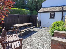 An outdoor patio area with a wooden picnic table and bench next to a white building with a small garden and wooden fence at The Cottage in Keswick