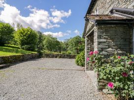 A stone house with a gravel driveway and flowers at Elterwater Lodge in Elterwater