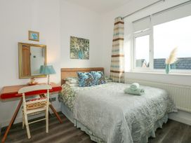A bedroom with a bed pillows a desk chair lamp mirror and window at Sea View in Penrhyn Bay