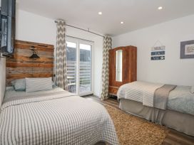 A bedroom with two single beds a wooden wardrobe sliding glass door and patterned curtains at Sea View in Penrhyn Bay