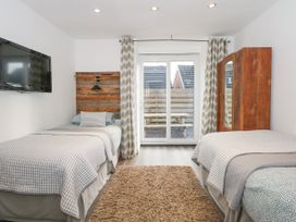 A bedroom with two single beds a wooden wardrobe a wall mounted tv and sliding glass doors at Sea View in Penrhyn Bay