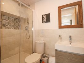 A bathroom with a shower enclosure a toilet a sink with a wooden framed mirror and a small wall decoration at Sea View in Penrhyn Bay