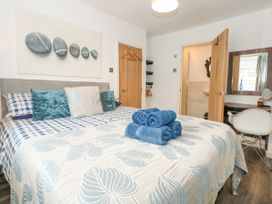 A bedroom with a bed covered in a leaf patterned bedspread and blue towels stacked on top at Sea View in Penrhyn Bay