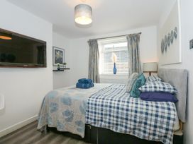 A bedroom with a bed with plaid and leaf patterned bedding a wall-mounted tv and a window with curtains at Sea View in Penrhyn Bay