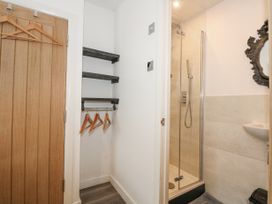 A small space with wooden hangers on black shelves next to a shower with glass doors and a decorative mirror at Sea View in Penrhyn Bay