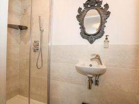 A bathroom with a shower area with glass doors, a small sink with a faucet, a soap dispenser, and a decorative mirror at Sea View in Penrhyn Bay