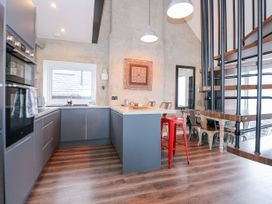 A kitchen with grey cabinets and a wooden floor next to a dining area with metal chairs and a red stool at Sea View in Penrhyn Bay