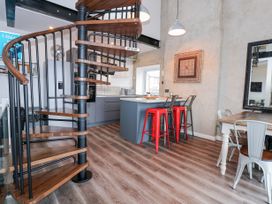 A kitchen area with a spiral staircase wooden bar stools and a dining table with metal chairs at Sea View in Penrhyn Bay