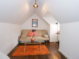 A small attic room with a beige sofa two patterned pillows an orange rug and a glass coffee table at Sea View in Penrhyn Bay