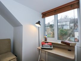 A small workspace with a wooden desk by a window with blinds a floor lamp a typewriter and a book at Sea View in Penrhyn Bay
