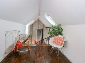 An attic sitting area with a wooden floor a wicker chair with a red throw a white chair with an orange geometric pillow and a plant at Sea View in Penrhyn Bay