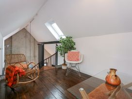 A sitting area with a rocking chair draped with a red blanket a modern white chair with an orange patterned cushion a potted plant and a glass table with a brown vase at Sea View in Penrhyn Bay