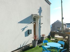 A small outdoor seating area with blue and beige chairs and tables next to a white wall of a house with two potted plants at Sea View in Penrhyn Bay