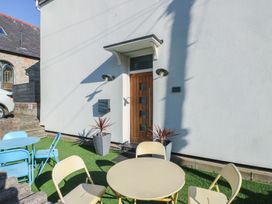 An outdoor seating area with round tables and chairs on artificial grass in front of a white building with a wooden door