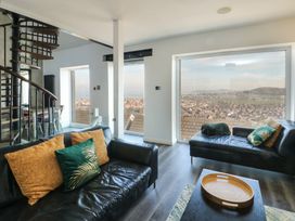 A living room with black leather sofas and large windows showing a view at Sea View in Penrhyn Bay