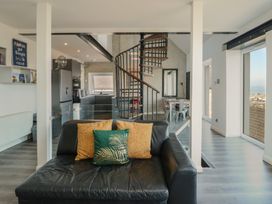 A black leather sofa with three cushions facing a kitchen with a spiral staircase and a dining area at Sea View in Penrhyn Bay