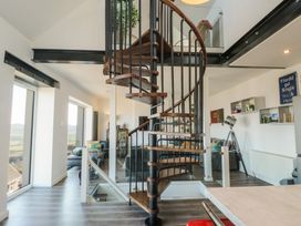 An interior space with a central spiral staircase surrounded by glass panels and windows a living area with chairs and shelves with books at Sea View in Penrhyn Bay