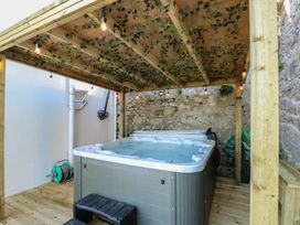 An outdoor hot tub under a wooden pergola with ivy and string lights on a wooden deck at Sea View in Penrhyn Bay