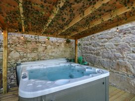 A hot tub under a wooden pergola with hanging lights and vines on the ceiling surrounded by stone walls at Sea View in Penrhyn Bay