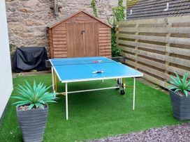 An outdoor area with a blue ping pong table two paddles and a ball a wooden shed a covered barbecue grill artificial grass two potted plants and a wooden fence at Sea View in Penrhyn Bay