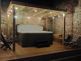 An outdoor wooden deck with a hot tub under a pergola with string lights and chairs against stone walls at Sea View in Penrhyn Bay