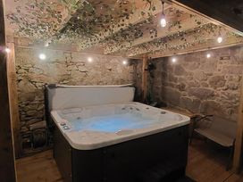 A hot tub with water and a cover in a stone wall room with wooden beams and hanging lights at Sea View in Penrhyn Bay