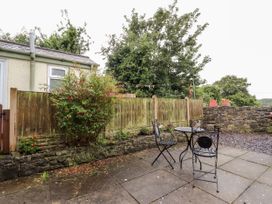An outdoor patio area with a small round table and two metal chairs next to a wooden fence and stone wall at Northgate Cottage in Ysceifiog near Caerwys
