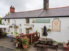 An outdoor seating area with wooden picnic tables and an umbrella outside a white building with signs advertising sunday roast and real ale at Northgate Cottage in Ysceifiog near Caerwys