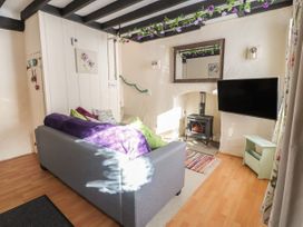 A living room with a grey sofa near a wood stove and a wall-mounted television at Northgate Cottage in Ysceifiog near Caerwys