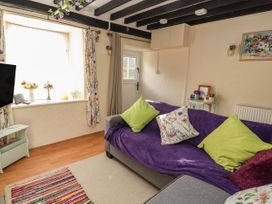 A living room with a gray sofa covered by a purple throw and green and floral cushions at Northgate Cottage in Ysceifiog near Caerwys