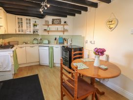 A kitchen with wooden table and chairs a stove dishwasher and shelves with decorations at Northgate Cottage in Ysceifiog near Caerwys