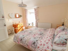 A bedroom with a bed with patterned bedding a wooden dresser and floral curtains at Northgate Cottage in Ysceifiog near Caerwys