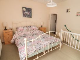 A bedroom with a metal bed with floral bedding two wooden bedside tables with lamps and a painting above the bed at Northgate Cottage in Ysceifiog near Caerwys